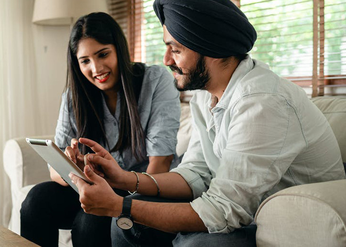 A couple sitting on a sofa, looking at a tablet device together.