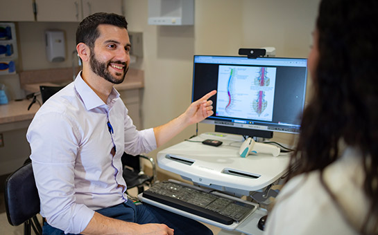 UC Davis Health rehabilitation specialist Shane Stone smiling and pointing at screen with spine diagram. 
