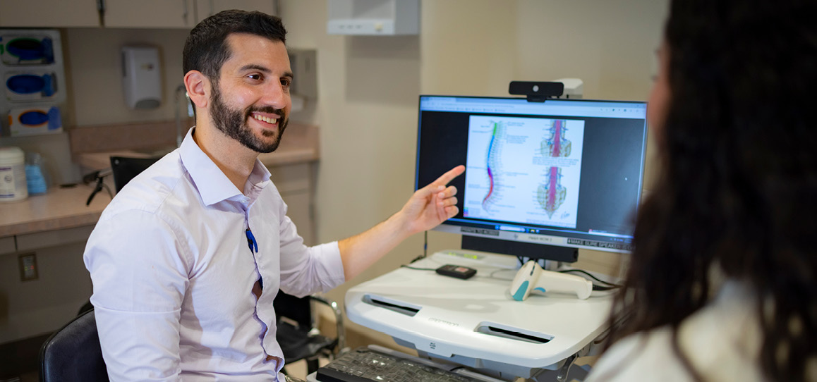 Physicial medicine and rehabilation physician Shane Stone smiling and pointing at a monitor next to patient.