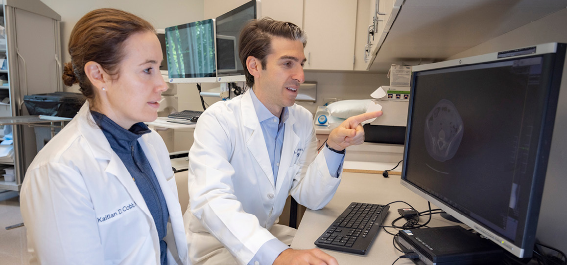 Urologists Kaitlan Cobb and Noah Canvasser looking at computer.