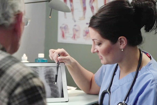 A healthcare worker pointing at an x-ray image, educating her patient.