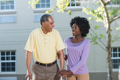 A woman assisting an elderly man using a walker