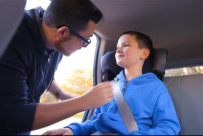 A man securing a child in a booster seat.