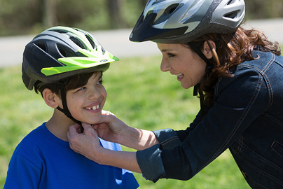 A mother tightening the straps on her child's helmet.