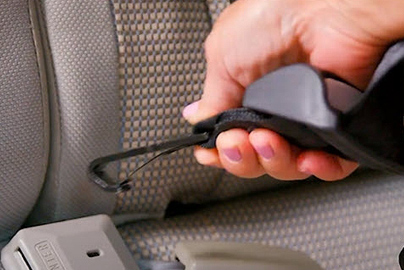 A hand holding a buckle about to attach it to a LATCH system anchor.