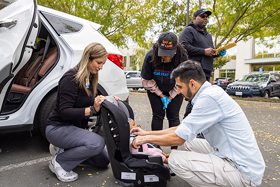 A couple with an instructor, placing a doll into a car seat.