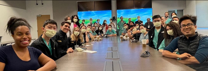 A large group of students and faculty sitting around a very large desk.