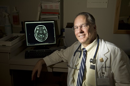 A researcher sits in front of a monitor showing brain scans