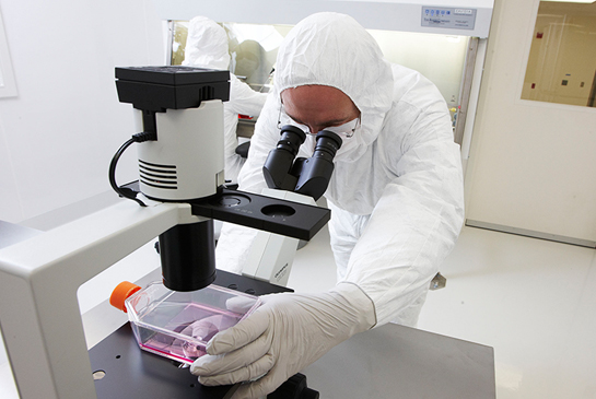 A person in full protective gear works with a microscope