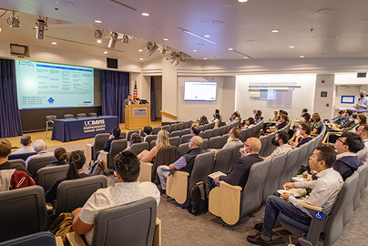 A group of people at a symposium, listening to a presenter.