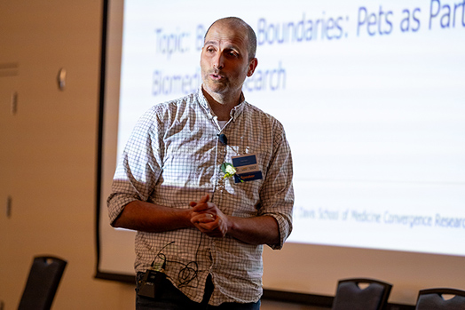 A man standing in a bright projected light speaking to an audience.