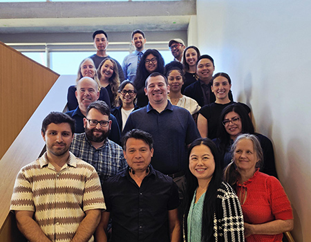 nineteen people stand together on various levels of a staircase and smile toward the camera