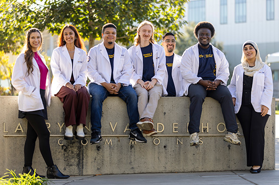 Medical school students sitting on School of Medicine sign, outdoor setting