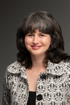 Professional photo of Bronwyn Seward Limon smiling at camera. Woman is wearing a black and white coat against a gray background.