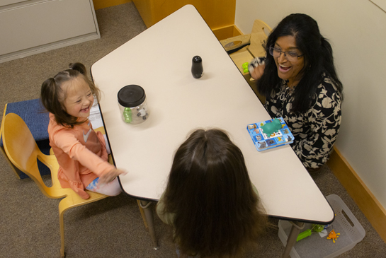 An adult interacting with two children seated at a table during a research study