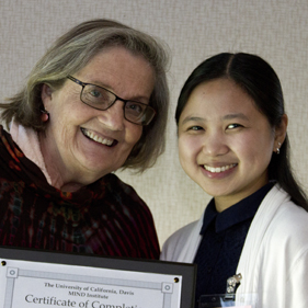 Two women smiling at the camera; one is holding a certificate of completion