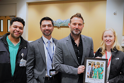 Three men and a woman pose while two of them hold a picture
