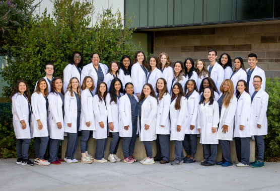 A group photo of OB-GYN residents outdoors dressed in white medical coats.