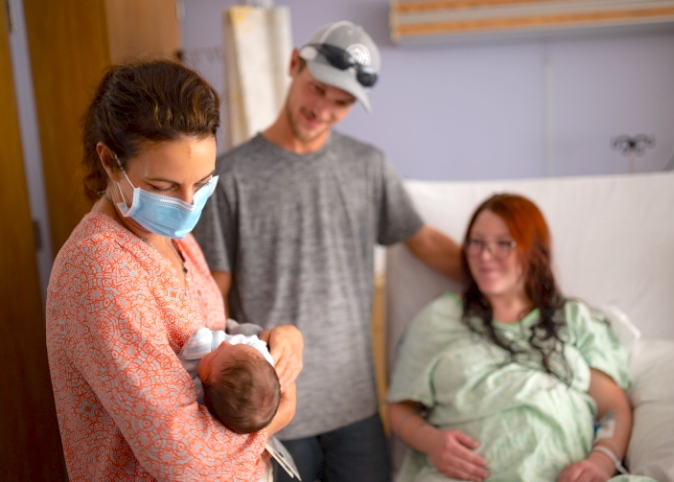 doctor holding newborn in delivery room as parents look on smiling