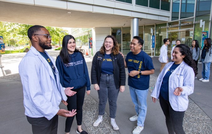 Four pediatrics clerkship students walk by UC Davis hospital signage.