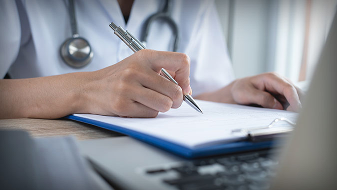 physician writing notes, with laptop