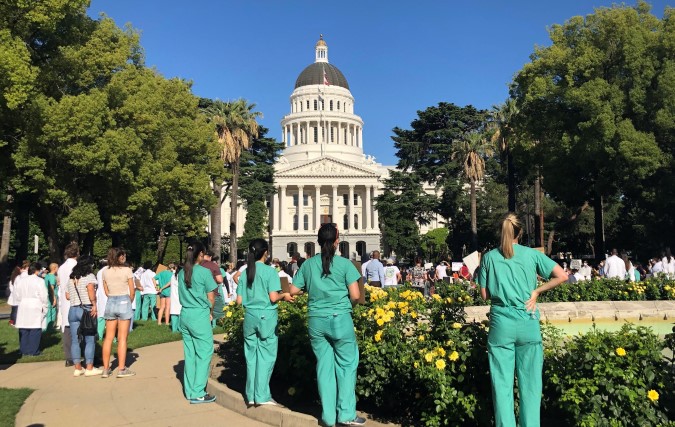 Residents gather in front of California capitol building all wearing green scrubs