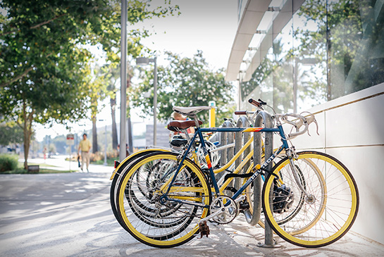 Blue bike with yellow rims locked up at campus bike rack with other bikes.