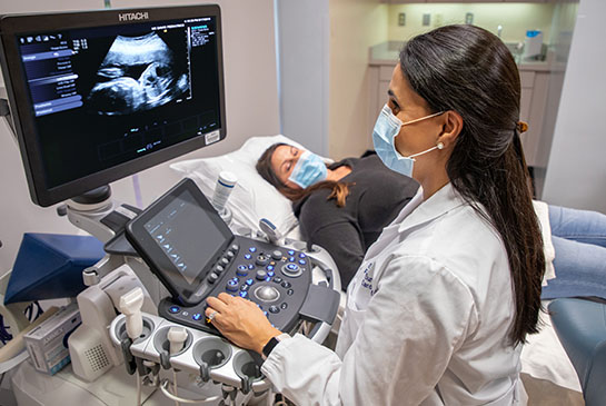 Doctor uses echogram on patient laying down in hospital bed.