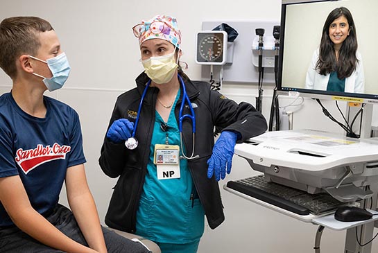 Nurse and teenage patient talk with doctor using telehealth.