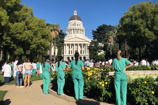 Residents in green scrubs and white coats gather in front of Capitol