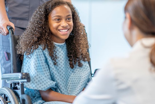 Young girl in wheelchair talks to doctor.