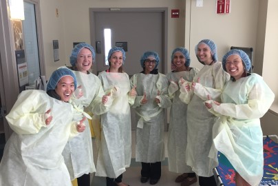 Doctors in yellow scrubs all pose in hospital hallway.