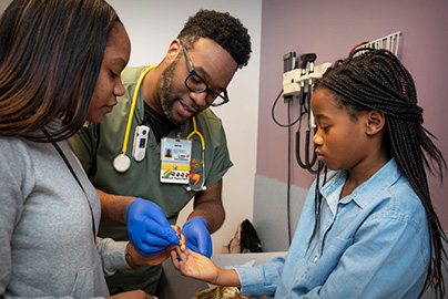 Doctor demonstrates blood test from finger with pediatric patient and mother.