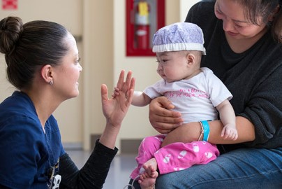 Mom holds baby in PICU while doctor examines baby.