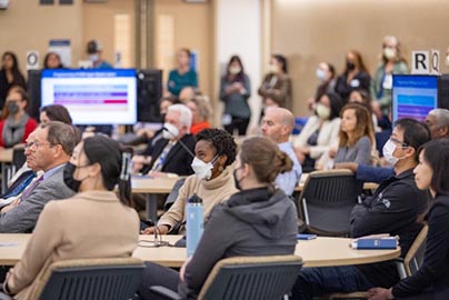 Many attendees in very large conference with people sitting at desks with monitors.