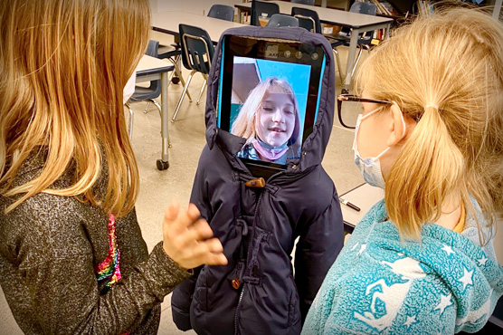 Two pediatric patients viewing small classroom robot with screen