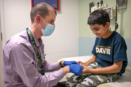 Dr. Crosses examines general pediatric patient sitting on hospital reclining chair.