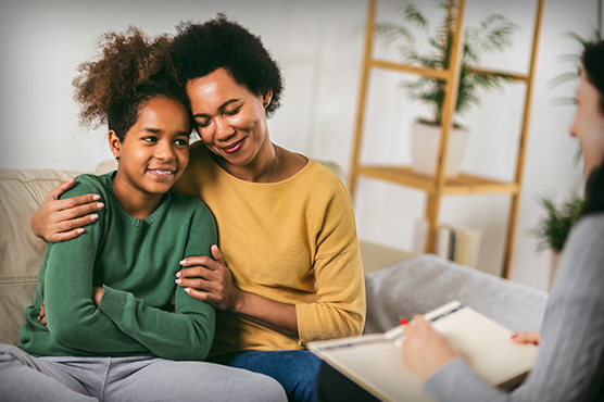 Mother hugs female adolescent patient while doctor advises.