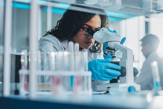 Research views slides with microscope in lab wearing blue gloves