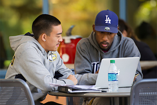Two students sitting at outside table looking at laptop