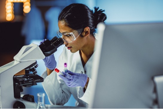 A woman looks into a microscope in a research lab