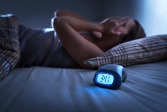 A woman lies awake next to an alarm clock