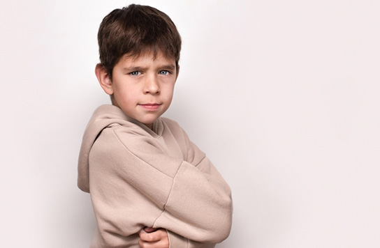 Young boy with crossed arms looking at camera, not smiling