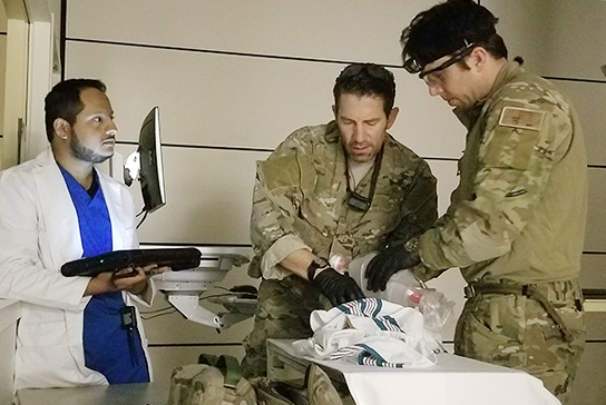 A healthcare worker with two armed forces personnel working on a operation simulation.