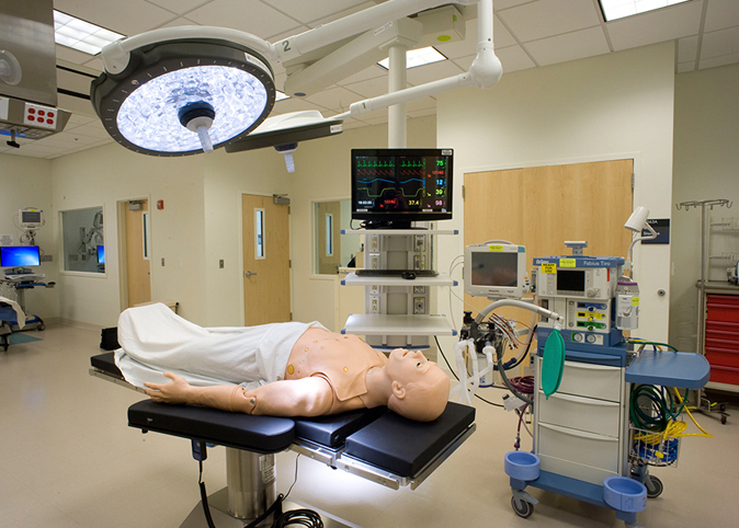 A full-bodied adult manikin is lying on an operating table in a medical simulation operating room.