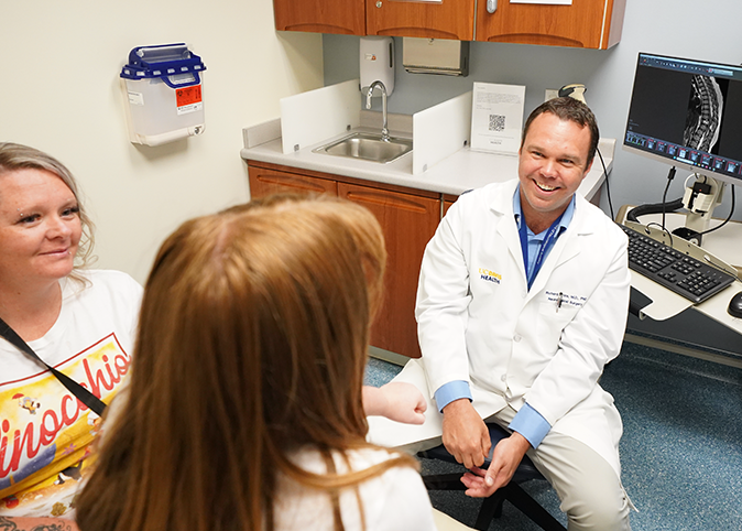 doctor smiling with patient and guardian looking at a spine xray on monitor