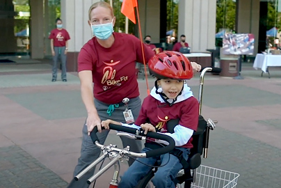 An adult helping a disabled child ride a tricycle, built for them.