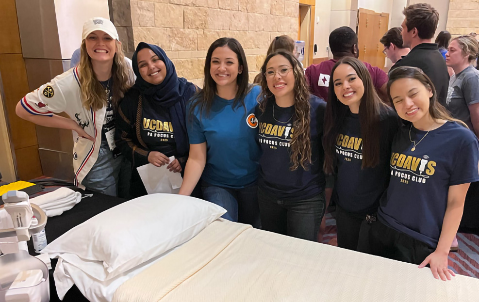 Group of students from the UC Davis PA POCUS Club smile and pose beside an ultrasound station during a hands-on skills competition.