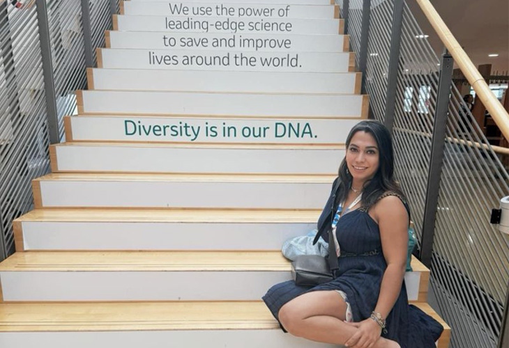 Person seated on a staircase featuring messages about science and diversity, posing beneath the phrase “Diversity is in our DNA.”