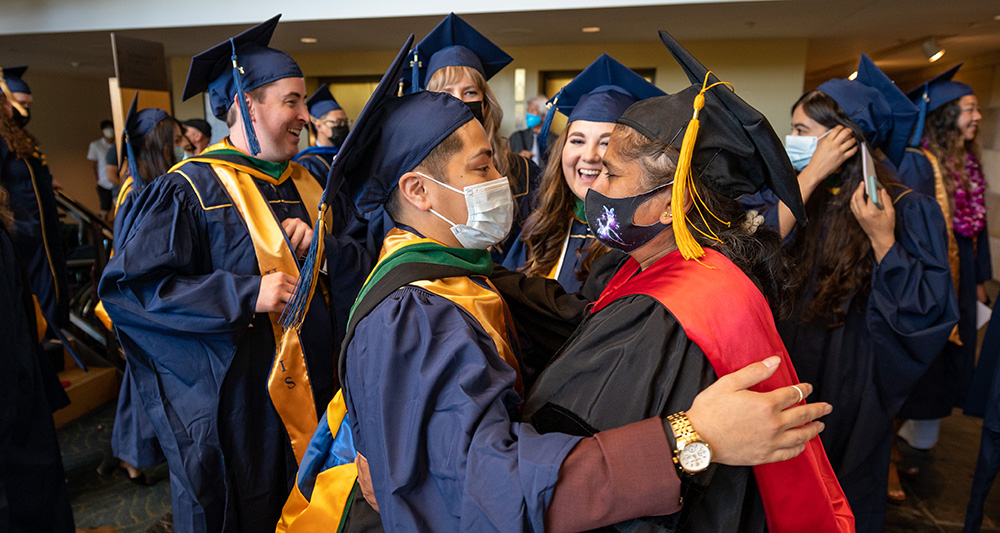 A Class of 2022 graduate celebrates with a hug with a faculty member.